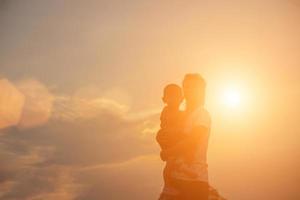 Silhouetten von Mutter und kleiner Tochter, die bei Sonnenuntergang spazieren gehen foto