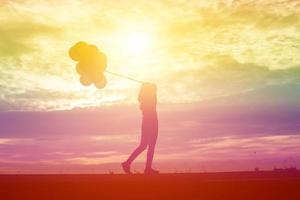 Silhouette einer jungen Frau, die bunte Luftballons mit Sonnenuntergang hält foto