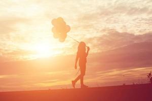 Silhouette einer jungen Frau, die bunte Luftballons mit Sonnenuntergang hält foto