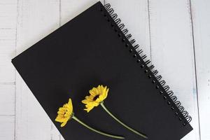 Schwarzes Notizbuch lag flach mit Sonnenblumen auf Holzschreibtisch. direkt darüber. foto