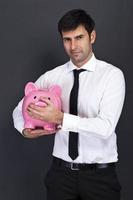 junger Mann mit Sparschwein (Sparbüchse), auf dunklem Hintergrund foto