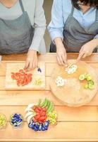 Zwei asiatische Frauen schneiden Knoblauch und Tomate mit einem Messer auf dem Holzbrett mit einer halben Limette Schlüsselblume Blume Schmetterling Erbse Frühlingszwiebel Erbsen und Eier in diesem Bereich und bereiten sich dann auf das Mittagessen vor. foto