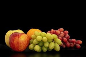 orange, trauben, apfel und pyrus pyriflora auf schwarzem hintergrund. foto