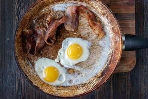 Hausgemachtes Frühstück mit Speck und Spiegeleiern in der Bratpfanne flach gelegt foto