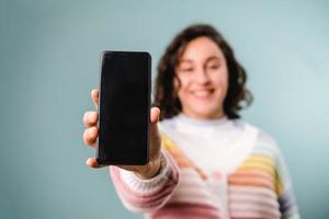 Frau, die ein Smartphone mit einem leeren Bildschirm in die Kamera zeigt, während sie vor einem isolierten Hintergrund steht. foto