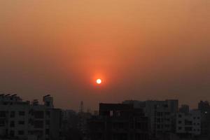 Abendsonnenuntergangfotografie auf Stadtbildhintergrund. Sonnenuntergangs- oder Sonnenaufgangsfoto eines städtischen Gebiets. Schöne und warme Sonnenuntergangslandschaft in Dhaka, Bangladesch. schöne rote Sonne vor der Morgendämmerung. foto