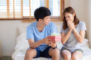 schönes junges asiatisches paar in der liebe überraschungsgeschenkbox im schlafzimmer zu hause, familienjubiläum mit genießen und romantisch zusammen ehefrau und ehemann mit beziehung, feiern valentinstag konzept. foto