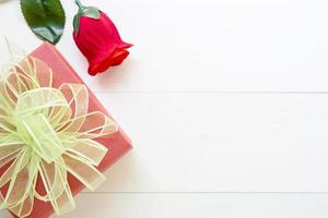 geschenk mit roter rosenblume und geschenkbox mit schleifenband auf holztisch, 14. februar des liebestages mit romantischem valentinstag-feiertagskonzept, draufsicht. foto