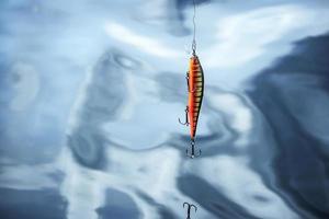 Angelköder Silber und roter Fisch mit gebrochenem Haken, der an einer Linie auf blauem Wasser hängt, natürlicher, unscharfer Hintergrund foto