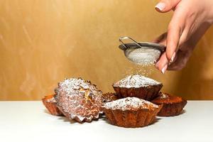 Eine Frau bestreut süße Cupcakes mit Puderzucker. foto