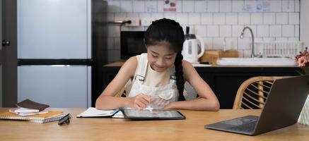 homeschool asiatisches kleines junges mädchen lernt online-unterricht vom schullehrer per remote-internet-meeting-anwendung aufgrund einer coronavirus-pandemie. Kind sucht Computer-Laptop-Bildschirm, den die Frau unterrichtet. foto