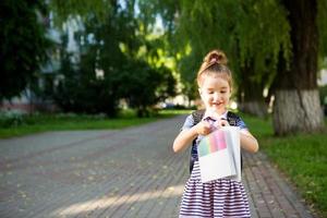 ein kleines mädchen mit kaukasischem aussehen in einer schuluniform mit einem rucksack und dem buch und einer reihe von markierungen. zurück zur Schule. Grundschule, Entwicklung von Aktivitäten für Kinder im Vorschulalter. Platz für Text foto