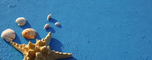 Rahmen mit Strandzubehör zu einem nautischen Thema Gelber Strohhut, Sonnenbrille, Seesterne und Muscheln auf blauem Hintergrund. Urlaubskonzept, Seereise, UV-Schutz, Schwimmen. Platz kopieren. flachgelegt foto