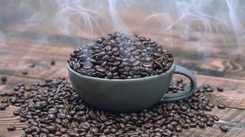 Tasse voller schwarzer Kaffeekörner liegen auf einem braunen Holztisch, Hintergrundbild. Kaffeebohnen in einer grünen Tasse. foto