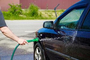Mann wäscht Auto im Freien. männliche hand hält schlauch mit wasser und wasserfahrzeug. foto