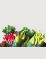 frisches grünes und rotes Chili-Designpaket aus biologischem Anbau, eingewickelt in Bananenblätter mit anderem Gemüse, das in weißem Hintergrund gestanzt ist foto