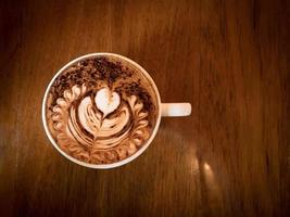 Cappuccino mit frischem Milchschaum und Latte Art in einem weißen Keramikglas auf einem Holztisch in einem Café. foto