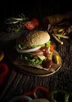 Hausgemachter Schweinefleisch-Hamburger mit gegrilltem Speck enthält Gemüse, Käse, Salat, Zwiebeln, Chili, Gewürze in einer Holzschale auf einem Holzboden. foto