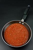 tomatensauce wird zubereitet, um als spaghetti oder pasta im italienischen stil in einer schwarzen pfanne auf schwarzem hintergrund gekocht zu werden.draufsicht foto