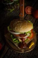 Hausgemachter Schweinefleisch-Hamburger mit gegrilltem Speck enthält Gemüse, Käse, Salat, Zwiebeln, Chili, Gewürze in einer Holzschale auf einem Holzboden. foto