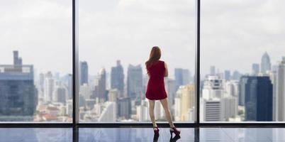 luxuriöse junge asiatische ceo-unternehmerin, die die skyline der innenstadt am fenster mit wolkenkratzer und stadtbild für visions- und immobilienentwicklungskonzept betrachtet foto