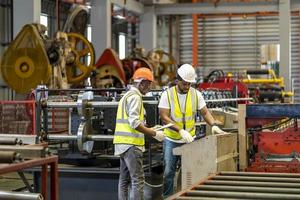 Ein Team von afroamerikanischen Industriearbeitern überprüft den Einrichtungswert der Blechrollformmaschine durch einen automatisierten Monitor, während sie in der Dachfabrik für das Konzept der Sicherheitsindustrie arbeitet foto