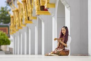 asiatische buddhistische frau liest sanskrit altes palmblattmanuskript von tripitaka, dem lord buddha dhamma, der lehrt, während sie am heiligen vollmondtag im tempel sitzt, um im kloster zu singen und anzubeten foto