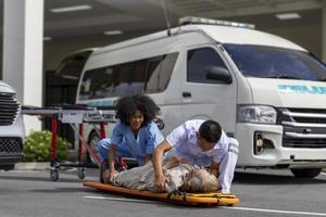 Das Sanitäterteam hilft dem älteren Patienten bei einem Autounfall, indem es das Rückenbrett verwendet, um es in den Krankenwagen für Erste-Hilfe- und Straßenunfallkonzepte zu überführen foto