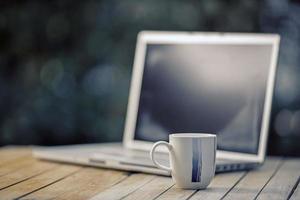 Kaffeetasse mit einem Computer-Laptop im grünen Naturhintergrund. remote oder von zu Hause aus arbeiten. weicher Fokus. flacher Fokuseffekt. foto