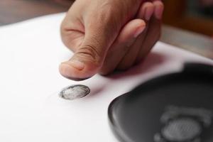 Personenhand, die schwarze Fingerabdrücke auf ein Papier legt, Nahaufnahme, foto