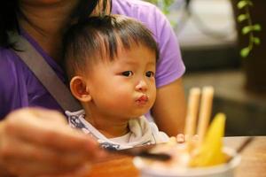 Mutter füttert ihren Sohn während des Abendessens im Restaurant mit Essen. asiatisches baby, das mit mutter isst. foto