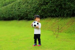 asiatischer junge, der ball in den händen im park hält. Kind, das Fußball spielt. foto