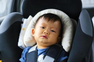 kleiner Junge weint, während er im Sicherheitsautositz befestigt ist. asiatisches kind, das mit dem auto reist. foto