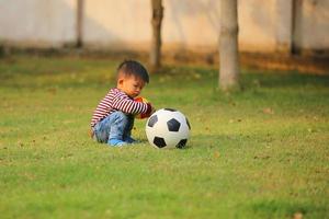 asiatischer Junge, der im Park Fußball spielt. Kind mit Bällen auf der Wiese. foto