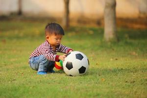 asiatischer Junge, der im Park Fußball spielt. Kind mit Bällen auf der Wiese. foto