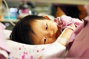 asiatisches baby hat fieber, wird dann ins krankenhaus eingeliefert und bekommt eine iv-röhre mit einem pad in den händen, um die medikamentennadel zu schützen. foto