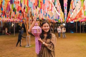 glückliche asiatische frau, die handgefertigte papierlaterne hält, um die jährliche laternenaufhängetradition in nordthailand nachts am phra that hariphunchai-tempel, lamphun, abzugeben foto