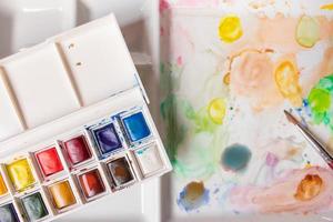 Schachtel mit Wasserfarben auf einer mit Farbe befleckten Palette foto