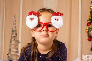kleines Mädchen mit Weihnachtsbrille und Grimassen foto