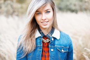 Porträt eines schönen Mädchens im Jeanskleid auf einem Hintergrund von Herbstgras foto