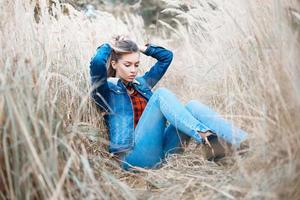 hübsche frau in einer jeansjacke und jeans, die im herbstgras sitzen. foto