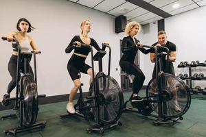 junge frauen trainieren auf luftfahrrädern im fitnessstudio mit motivierendem trainer. foto