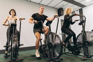 junger mann und frauen, die air bike für cardio-training im cross-trainingsstudio verwenden foto