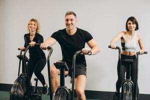 junger mann und frauen, die air bike für cardio-training im cross-trainingsstudio verwenden foto