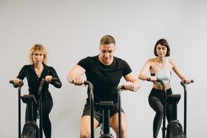 junger mann und frauen, die air bike für cardio-training im cross-trainingsstudio verwenden foto