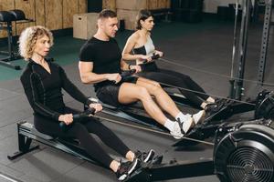 junger Mann und schöne Frauen trainieren mit Rudergerät im Crossfit-Fitnessstudio. foto