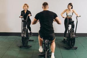 junger mann und frauen, die air bike für cardio-training im cross-trainingsstudio verwenden foto