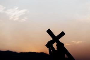 Silhouette eines Mannes, der bei Sonnenuntergang ein Kreuz trägt. Begriff der Religion. foto