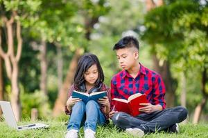 Junge und Mädchen lesen ein Buch, Bruder und Schwester sitzen auf dem Gras und lesen das Buch im Park, Kinder spielen Lernkonzepte im Freien foto