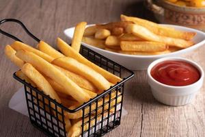 Pommes Frites in einem schwarzen Korb mit Tomatensauce foto